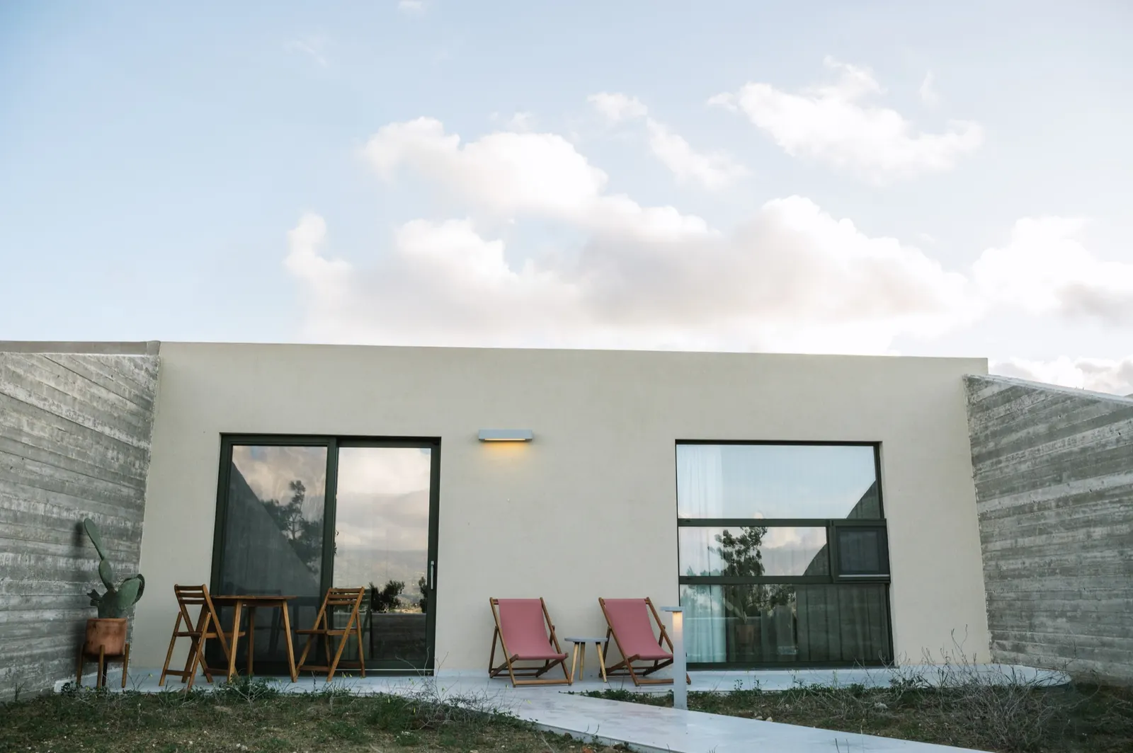 Lower Guesthouse facade between board-formed concrete wings, deck chairs on the patio